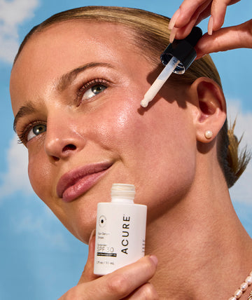 Woman applying Acure Sun serum drops – clean SPF for glowing, protected skin.